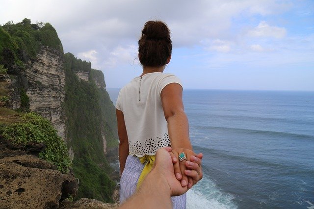 Žena drží za ruku muža na útese nad morom a pri skalách.jpg